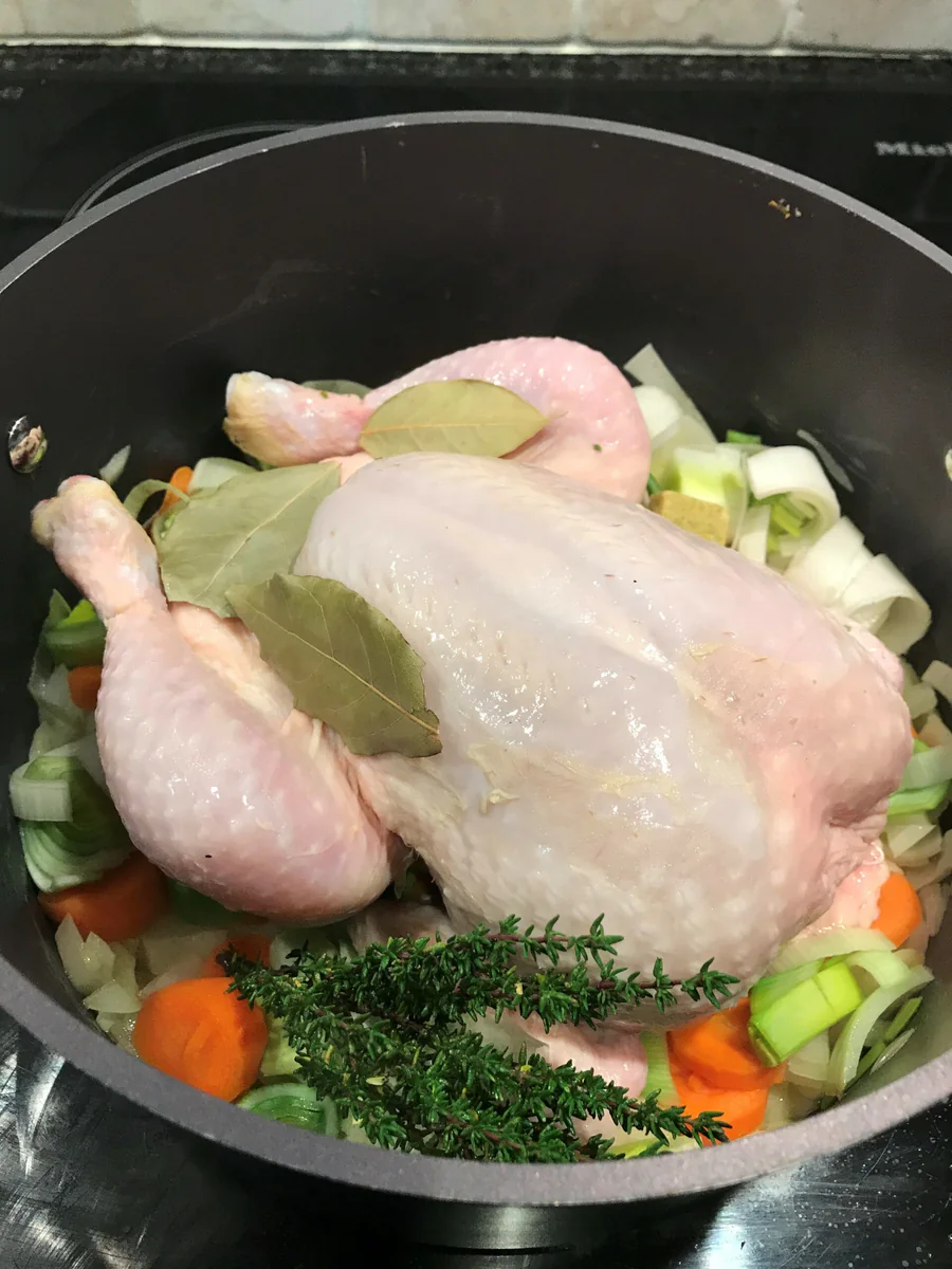 Ganzes Hähnchen mit Gemüse und Lorbeer in einem Kochtopf.