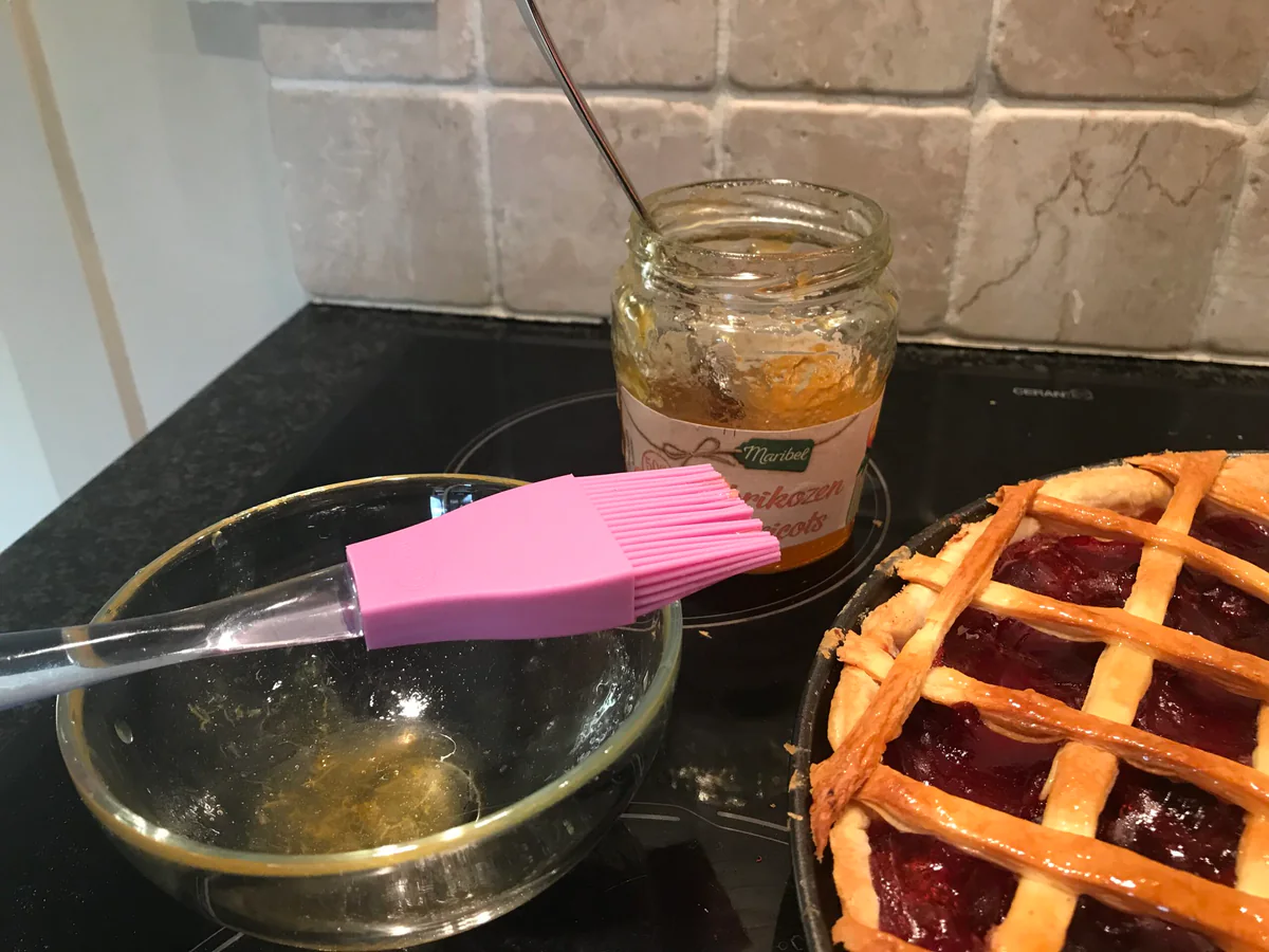 Baked cherry tart with a jar of glaze and a brush.