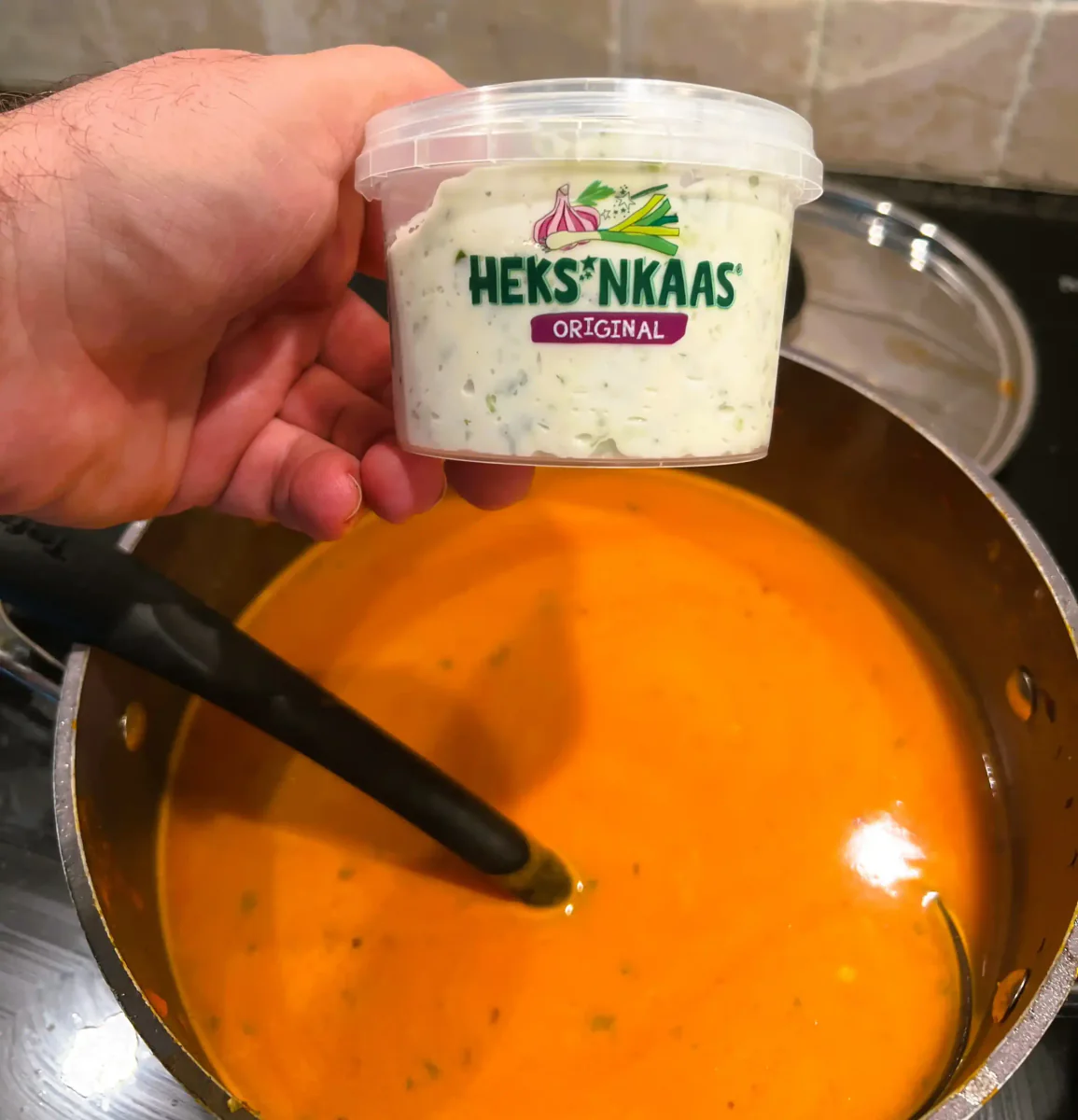 Becher Kräuterfrischkäse über einem Topf Tomatensuppe.