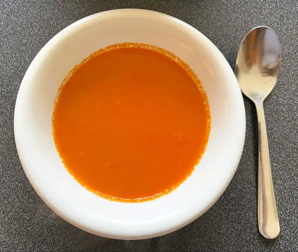 Schüssel glatte Tomatensuppe mit einem Löffel daneben.