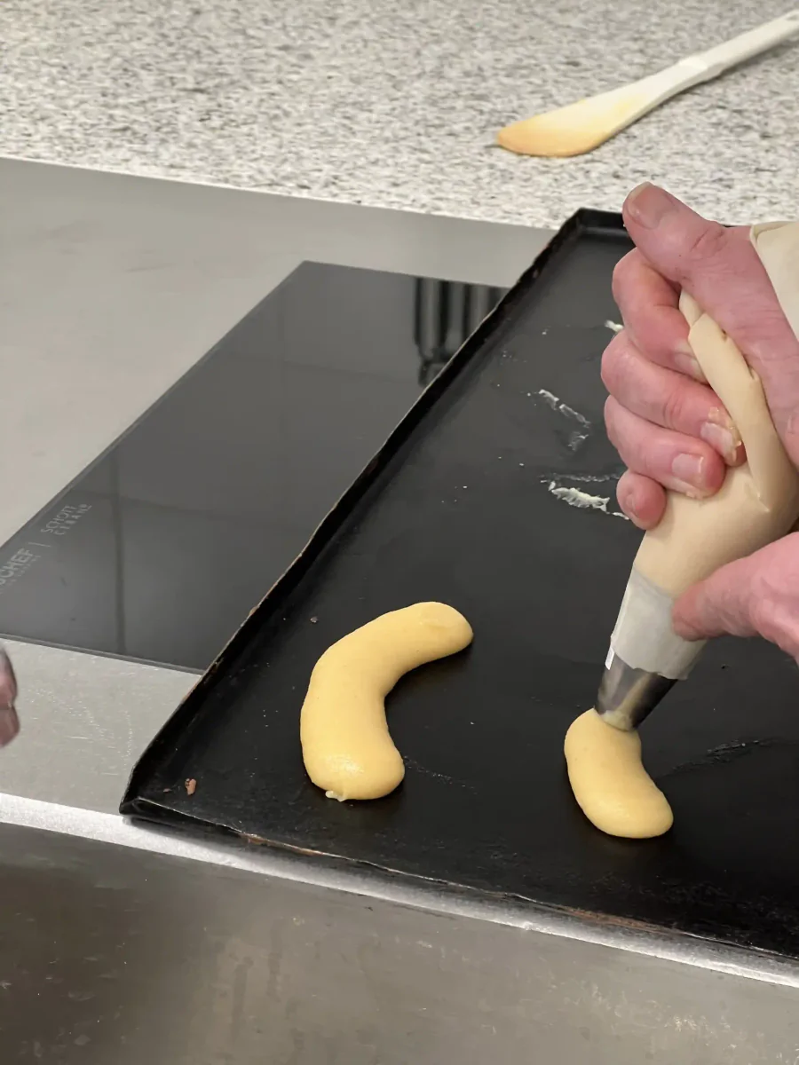 Halvemaanvormen van soezendeeg op een bakplaat spuiten.