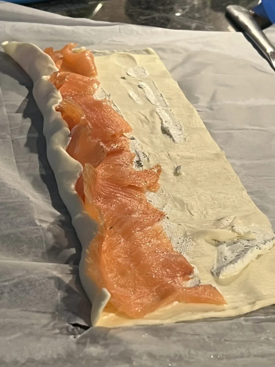 Rectángulo de hojaldre con queso de hierbas y salmón, parcialmente enrollado.