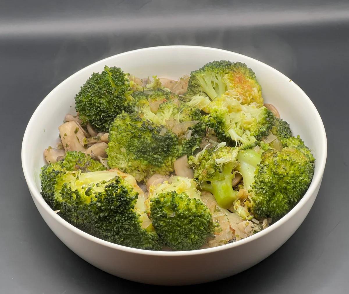 Geroerbakte broccoli met champignons in een pan, afgewerkt met een vleugje peper en peterselie, onder warme keukenbelichting.
