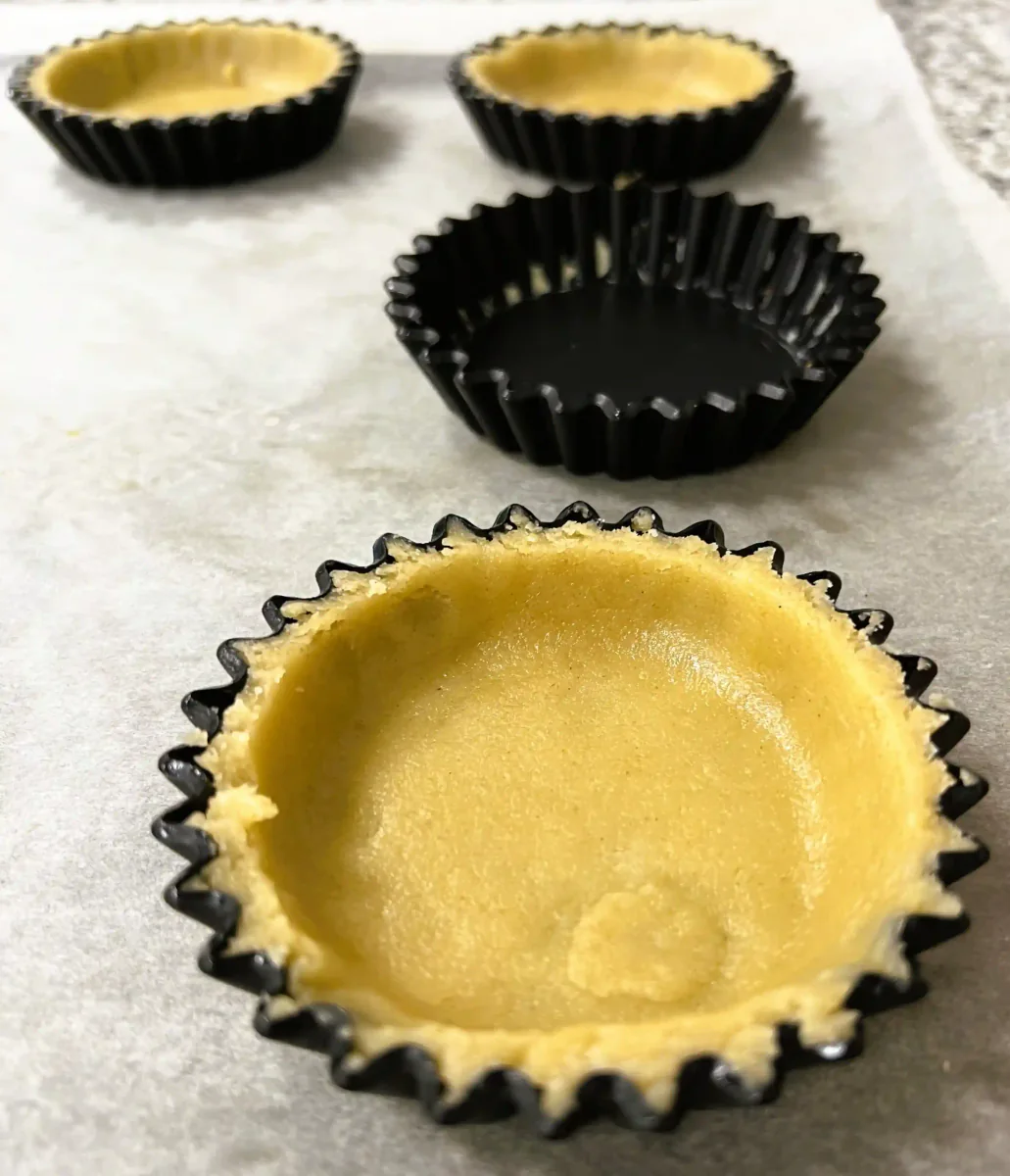 Lining small tart tins with pastry.