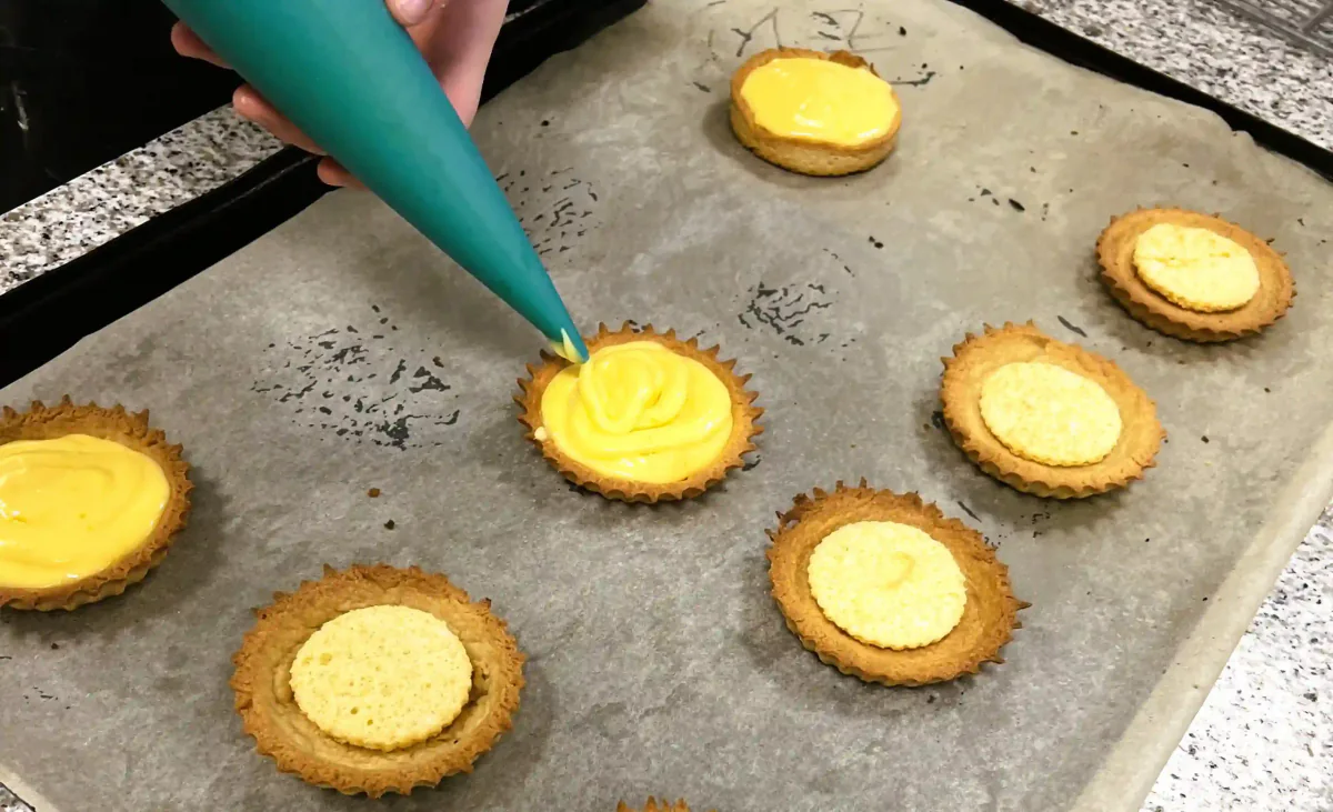 Piping lemon cream into small tart cases.