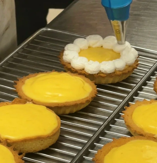 Piping white meringue around the edges of lemon tartlets.