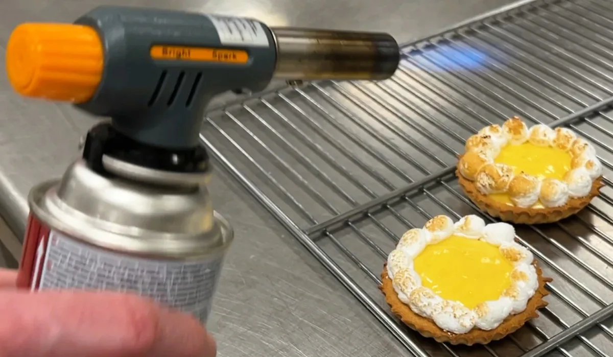 Browning the meringue on lemon tartlets with a kitchen torch.