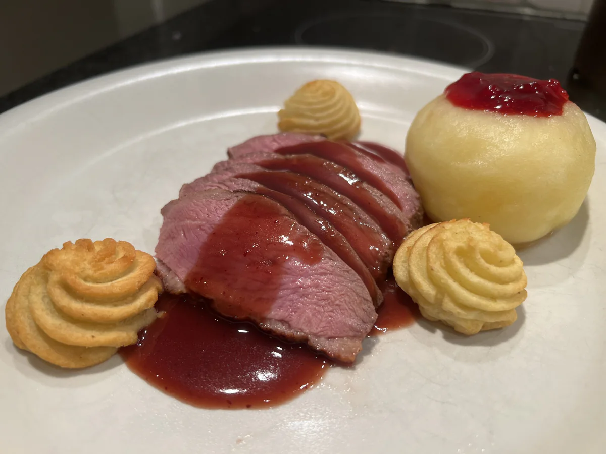 Sliced duck breast with sauce, potatoes and a stuffed apple.