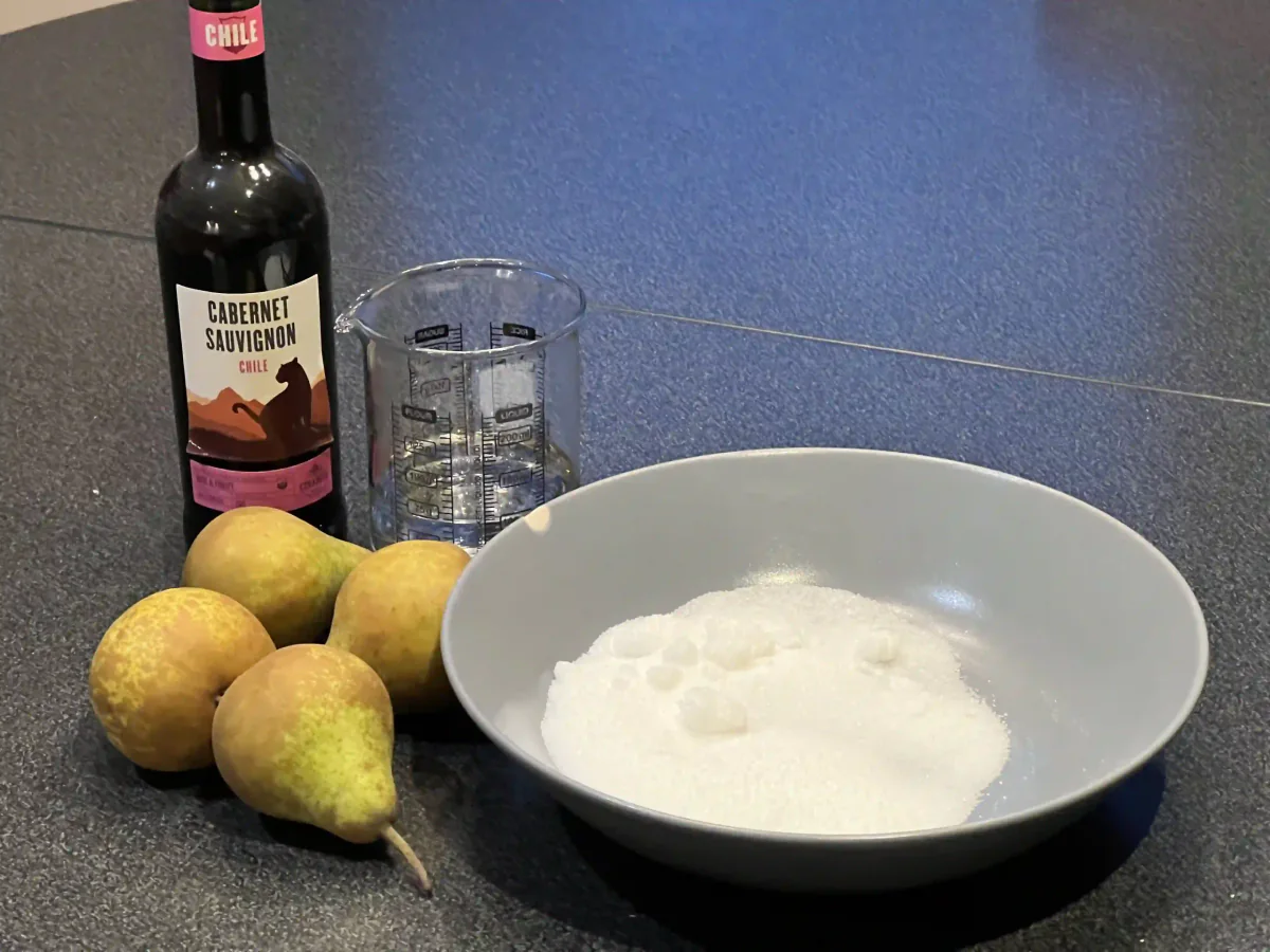 Pears, sugar and a bottle of red wine on the kitchen counter.