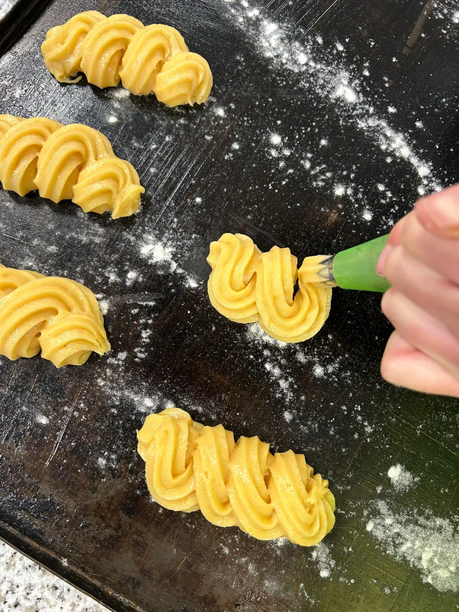 Piping ridged strips of choux pastry onto a baking tray.