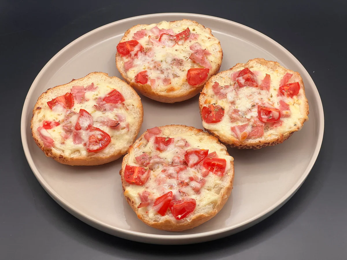 Vier Brötchenhälften mit Tomate, Schinken und geschmolzenem Mozzarella — Brötchenpizzas frisch aus dem Ofen