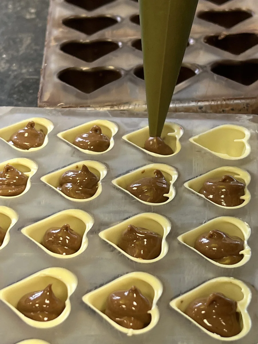 Piping filling into heart-shaped chocolates.