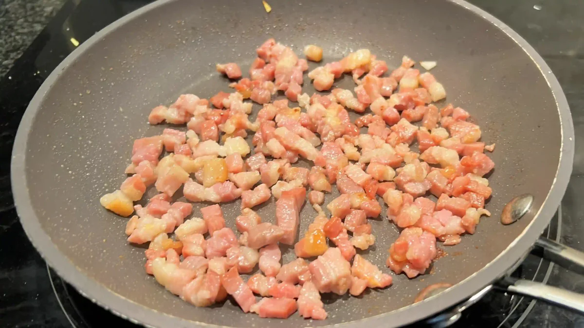 Frying diced bacon in a pan.