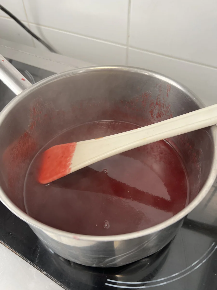 Heating a red fruit mixture in a saucepan.
