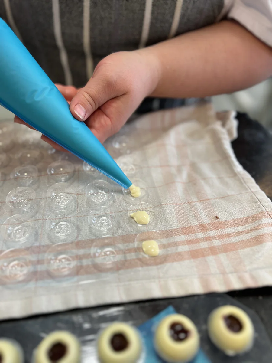 Piping filling into small hollow chocolate spheres.