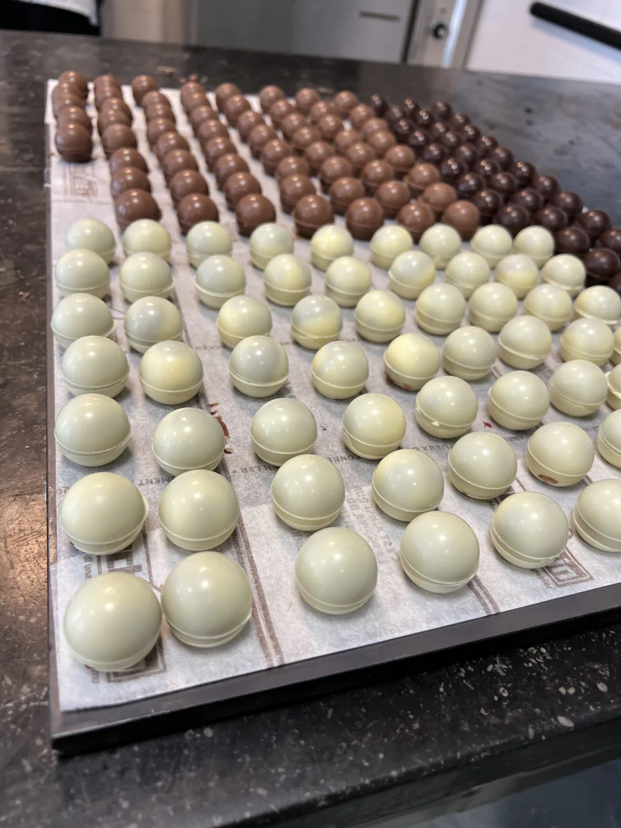 Filled white and dark chocolate spheres on a baking tray.