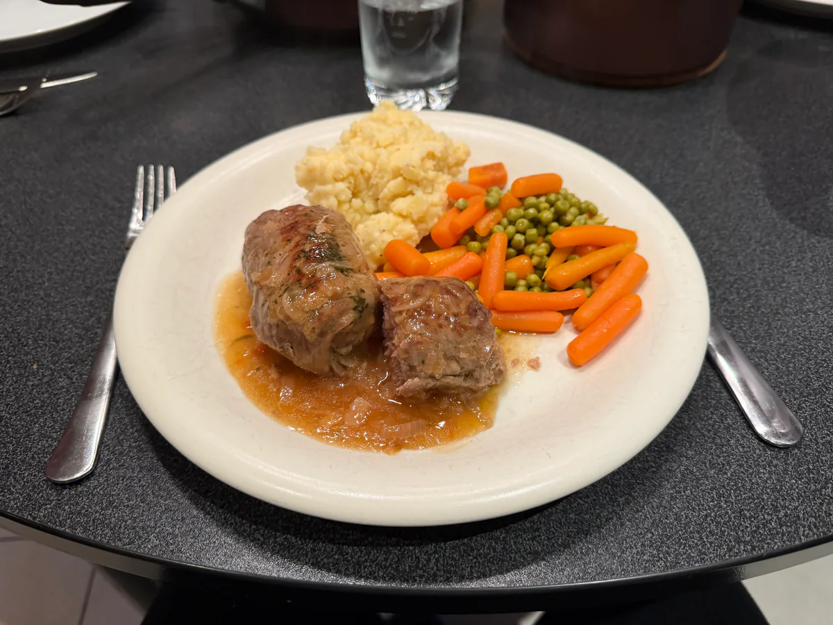 Het volledige bord met vogels zonder kop, bruine uiensaus, puree, erwten en wortelen.
