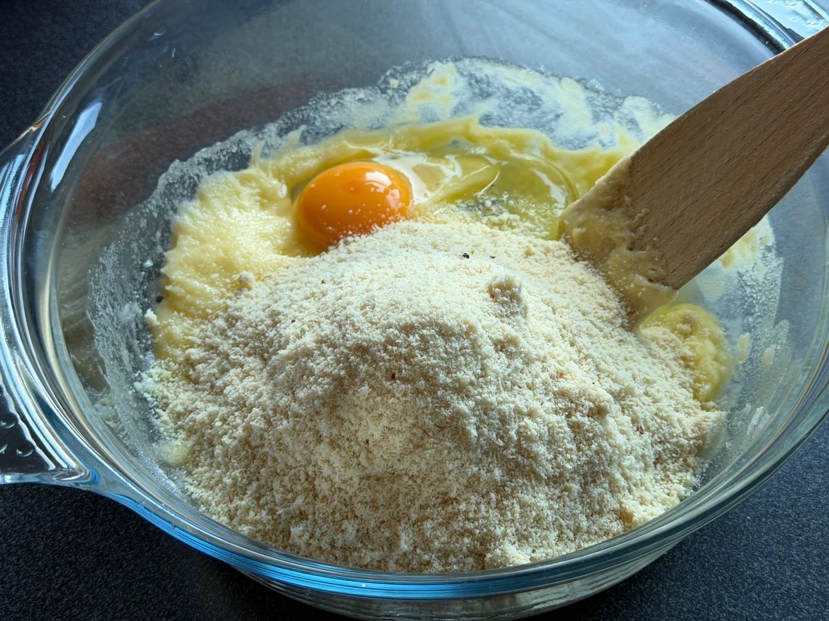 Amandelpoeder en een ei bij het boter-suikermengsel in de mengkom