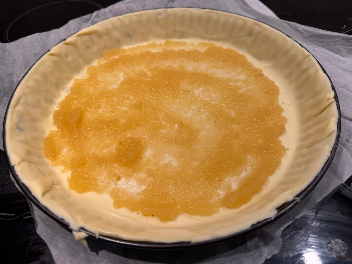 Een dunne laag appelmoes op het bladerdeeg in de taartvorm