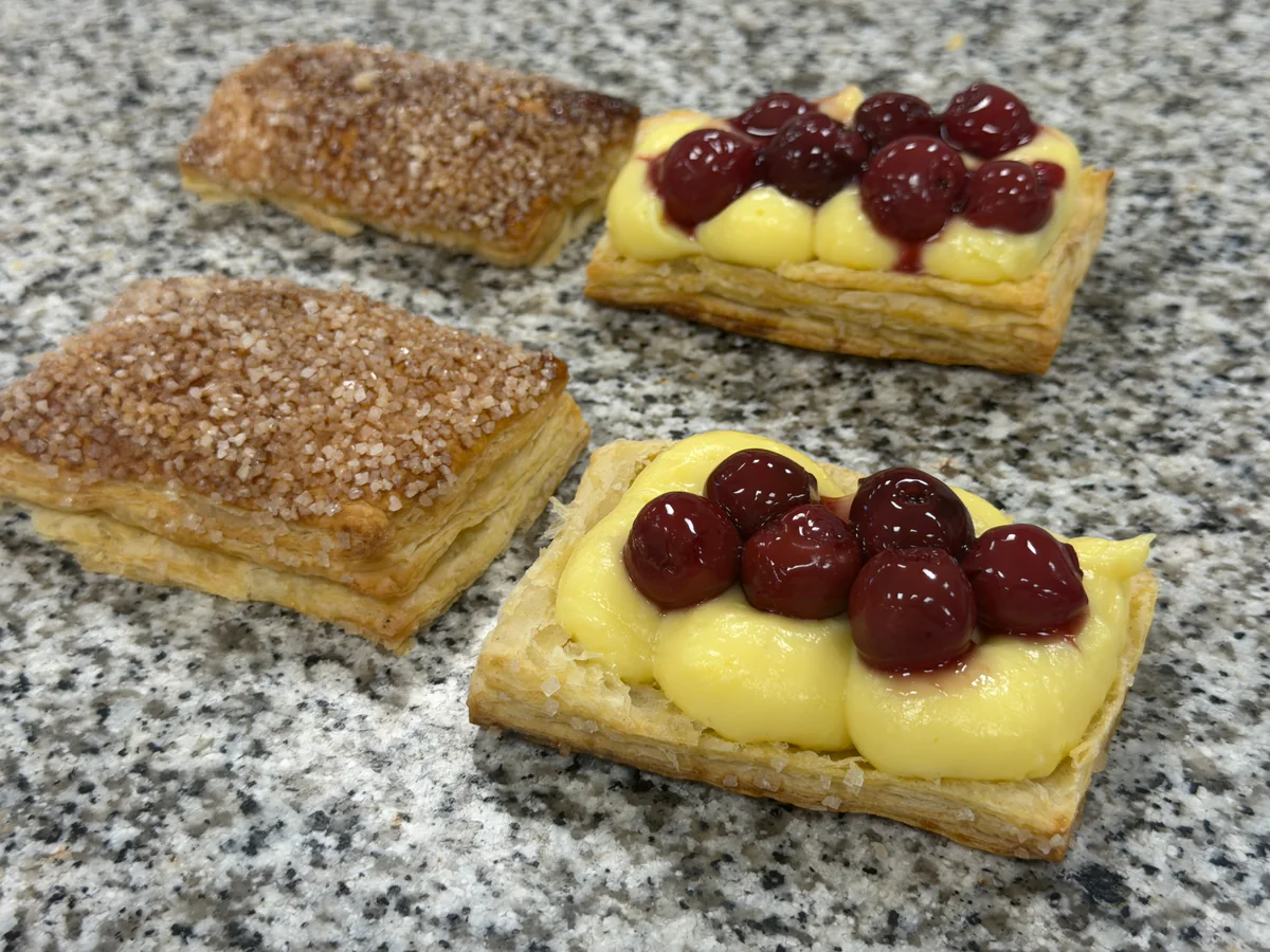 Sauerkirschen liegen in der Mitte auf der Konditorcreme, mit den Hauben daneben.