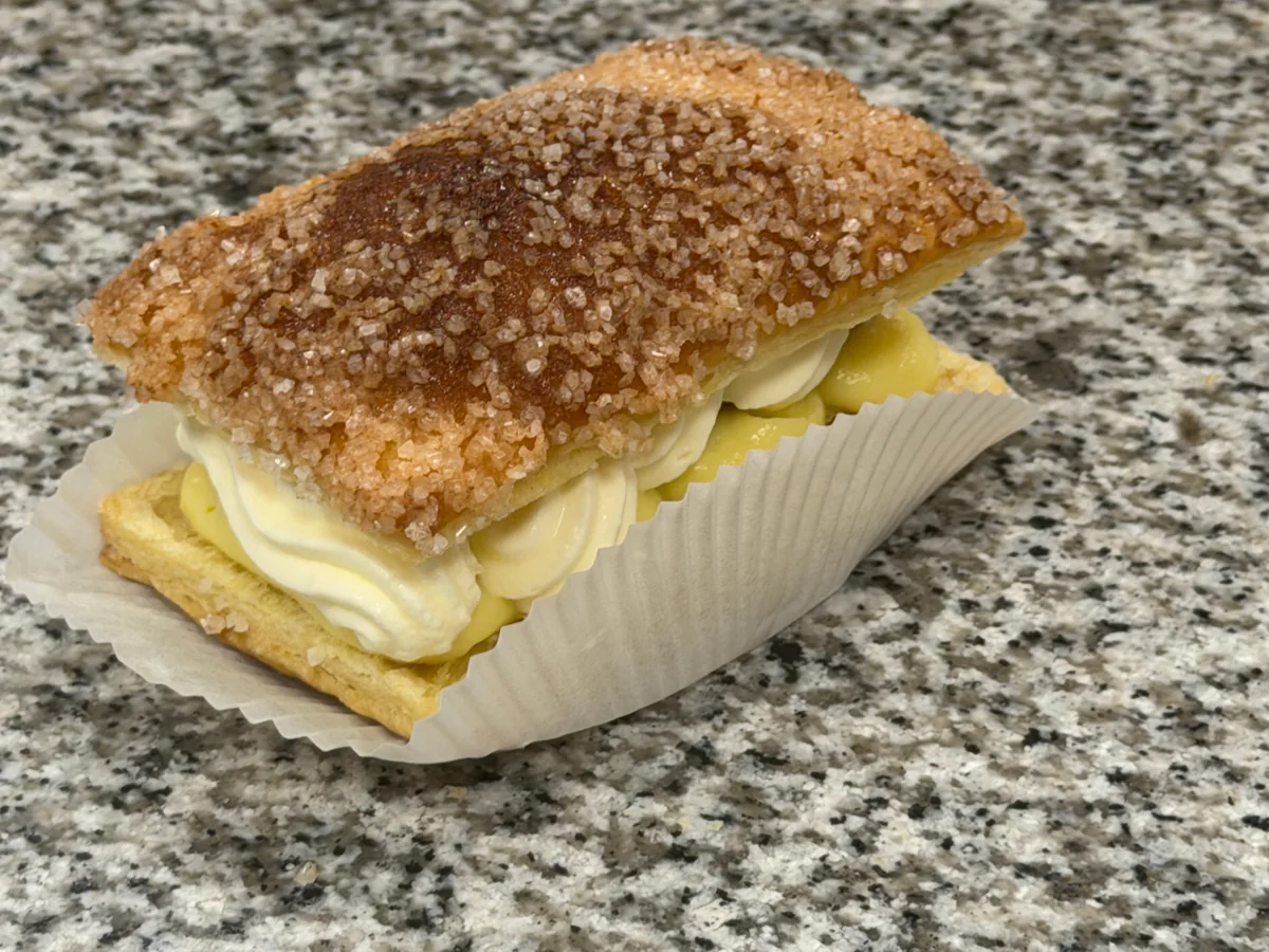 Fertige Allumette mit Konditorcreme, Sauerkirschen und Schlagsahne unter einer gezuckerten Blätterteighaube.