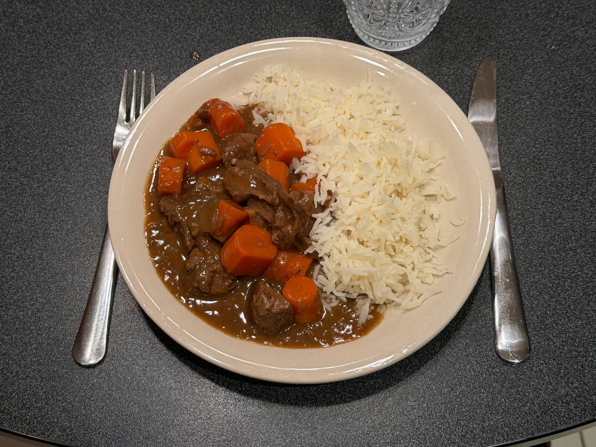 Opgediend bord hertenragout met wortelen en bruine saus naast rijst.