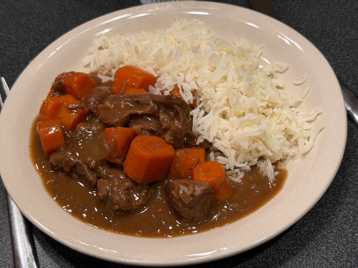 Hertenragout met wortelen in bruine saus, geserveerd met rijst op een bord.