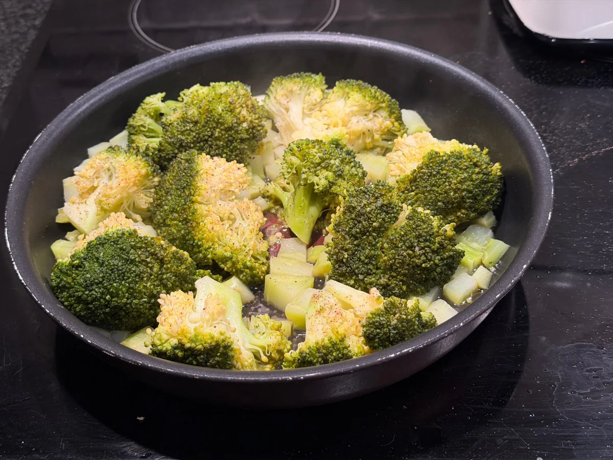Broccoliroosjes en stukjes stronk gestoofd in een braadpan.