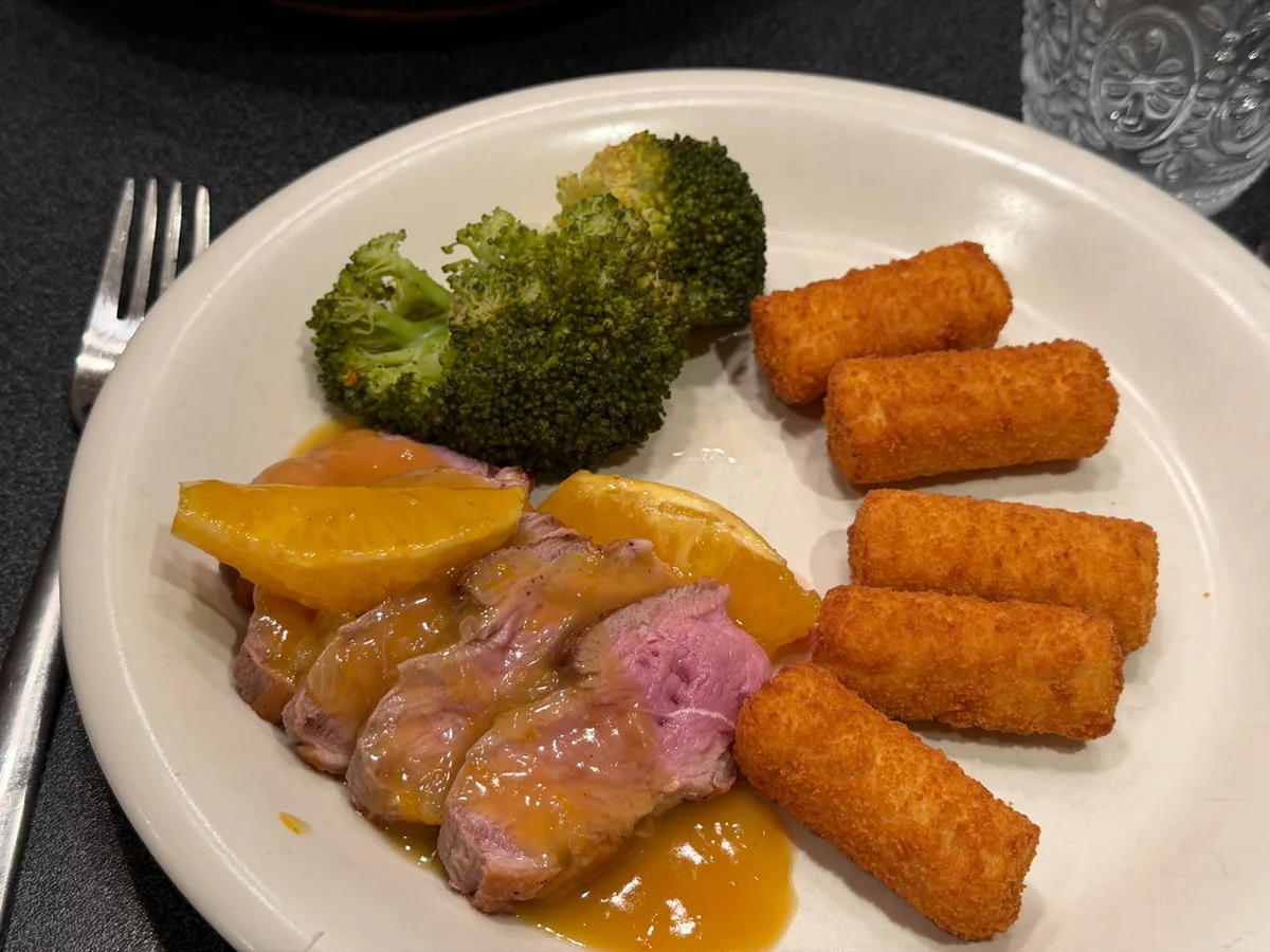 Eigen bordfoto van eendenborst met appelsiensaus, broccoli en aardappelkroketten.