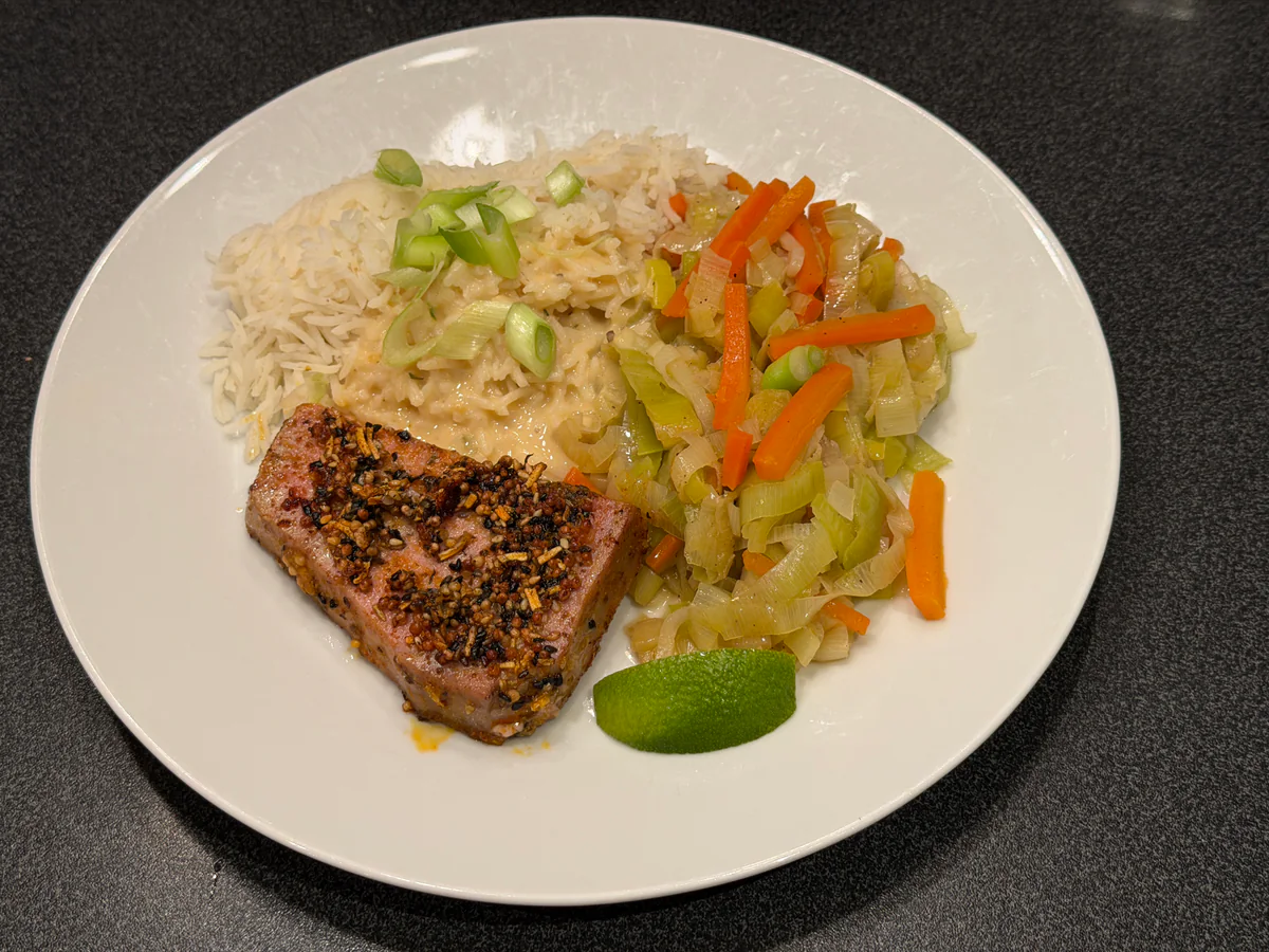 Teriyakitonijn met rijst, saus, gestoofde prei en wortelen, afgewerkt met lente-ui en limoen.