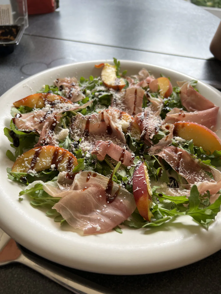 Eine Harmonie aus Prosciutto, frischem Pfirsich und Parmesan oder Feta auf Rucola mit süßer Balsamicocreme