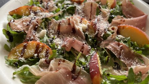 en harmonie van prosciutto, verse perzik, en Parmezaan (of Feta) op een bedje van rucola, afgemaakt met een zoete balsamico crème.