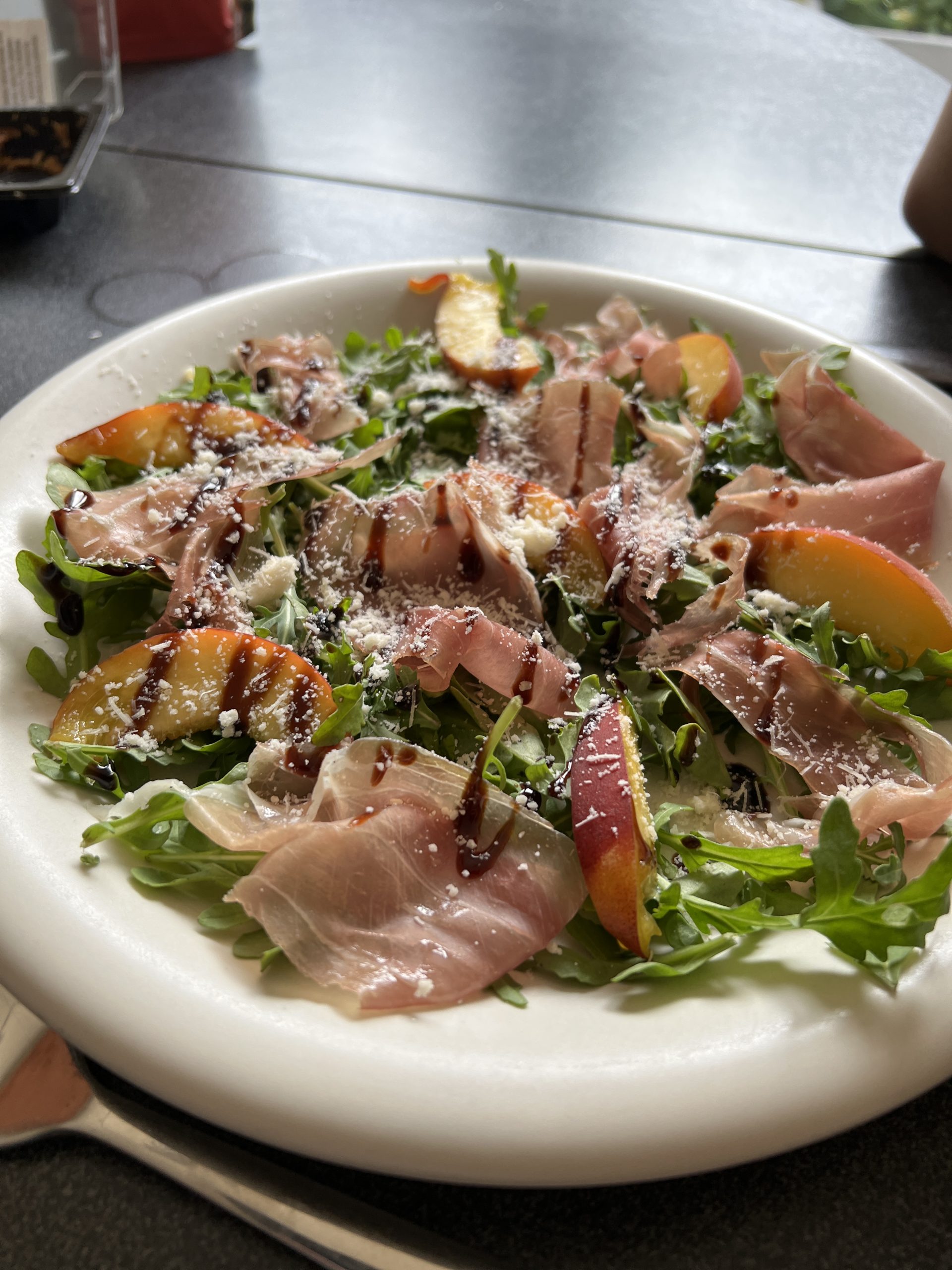 en harmonie van prosciutto, verse perzik, en Parmezaan (of Feta) op een bedje van rucola, afgemaakt met een zoete balsamico crème.