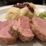 Varkenshaasje versneden op het bord met een portie broccoli en puree met rode bessen saus