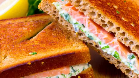 A Croque Norvégien sandwich, featuring two slices of toasted whole wheat bread. The sandwich is made with smoked salmon and herb cream cheese.