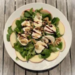 Topaanzicht frisse salade met geitenkaas, appel, walnoten en balsamico op een wit bord