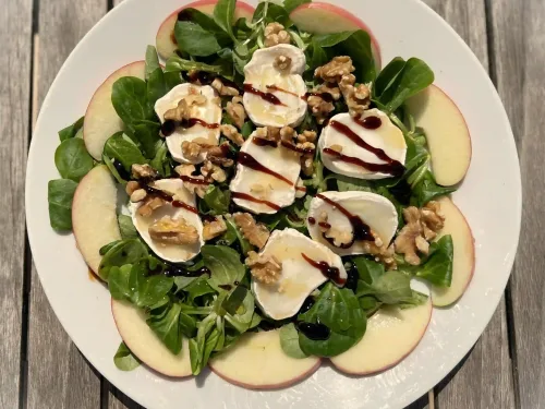 Topaanzicht frisse salade met geitenkaas, appel, walnoten en balsamico op een wit bord