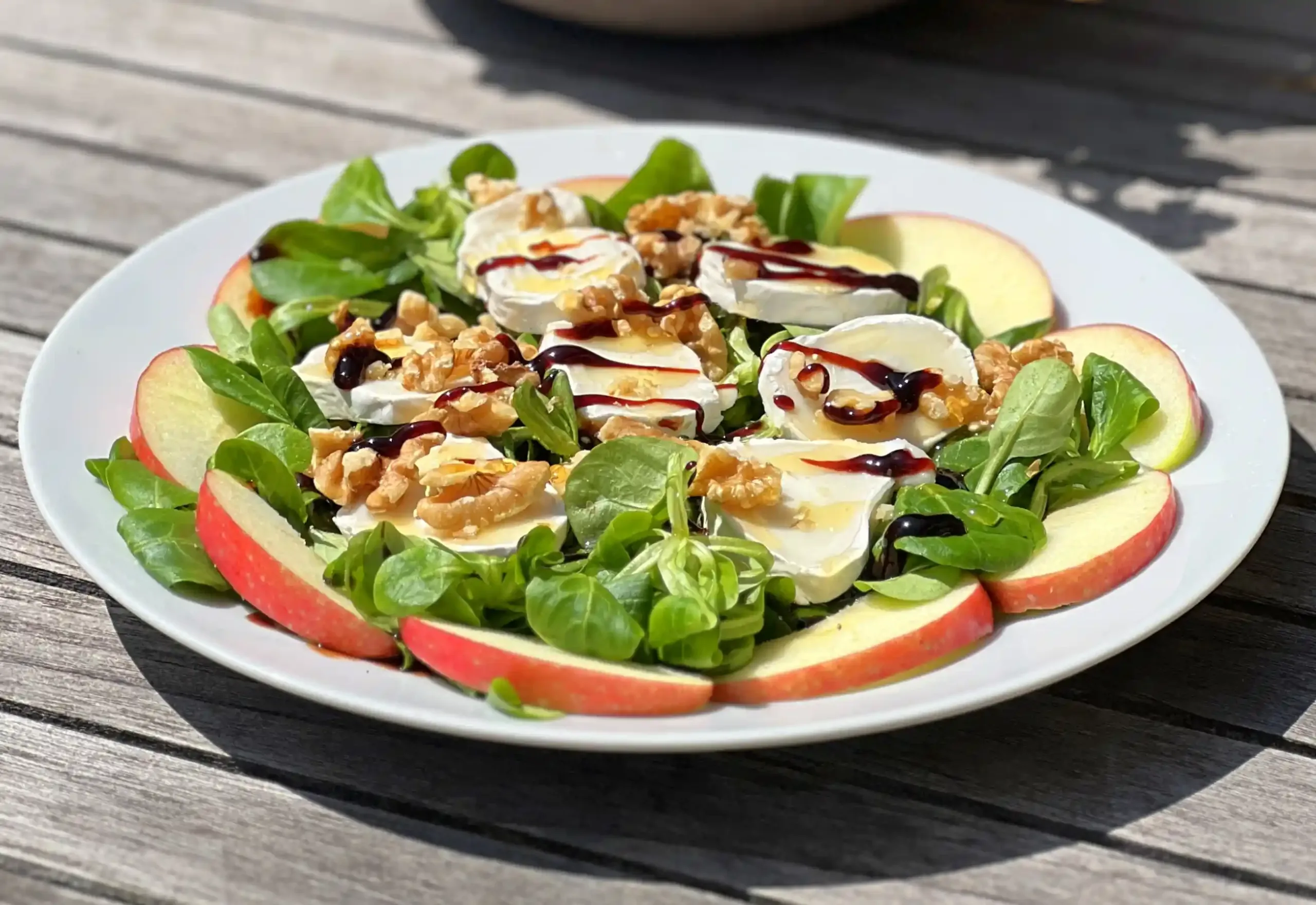 Frisse salade met geitenkaas, appel, walnoten en balsamico op een wit bord