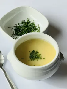 Kommetje romige aspergesoep met verse bieslook erover gestrooid, geserveerd op witte achtergrond