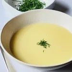 Bord romige aspergesoep met verse bieslook erover gestrooid, geserveerd op witte achtergrond