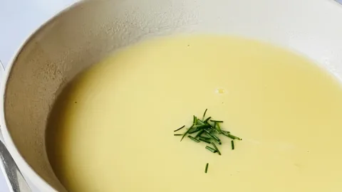 Bord romige aspergesoep met verse bieslook erover gestrooid, geserveerd op witte achtergrond