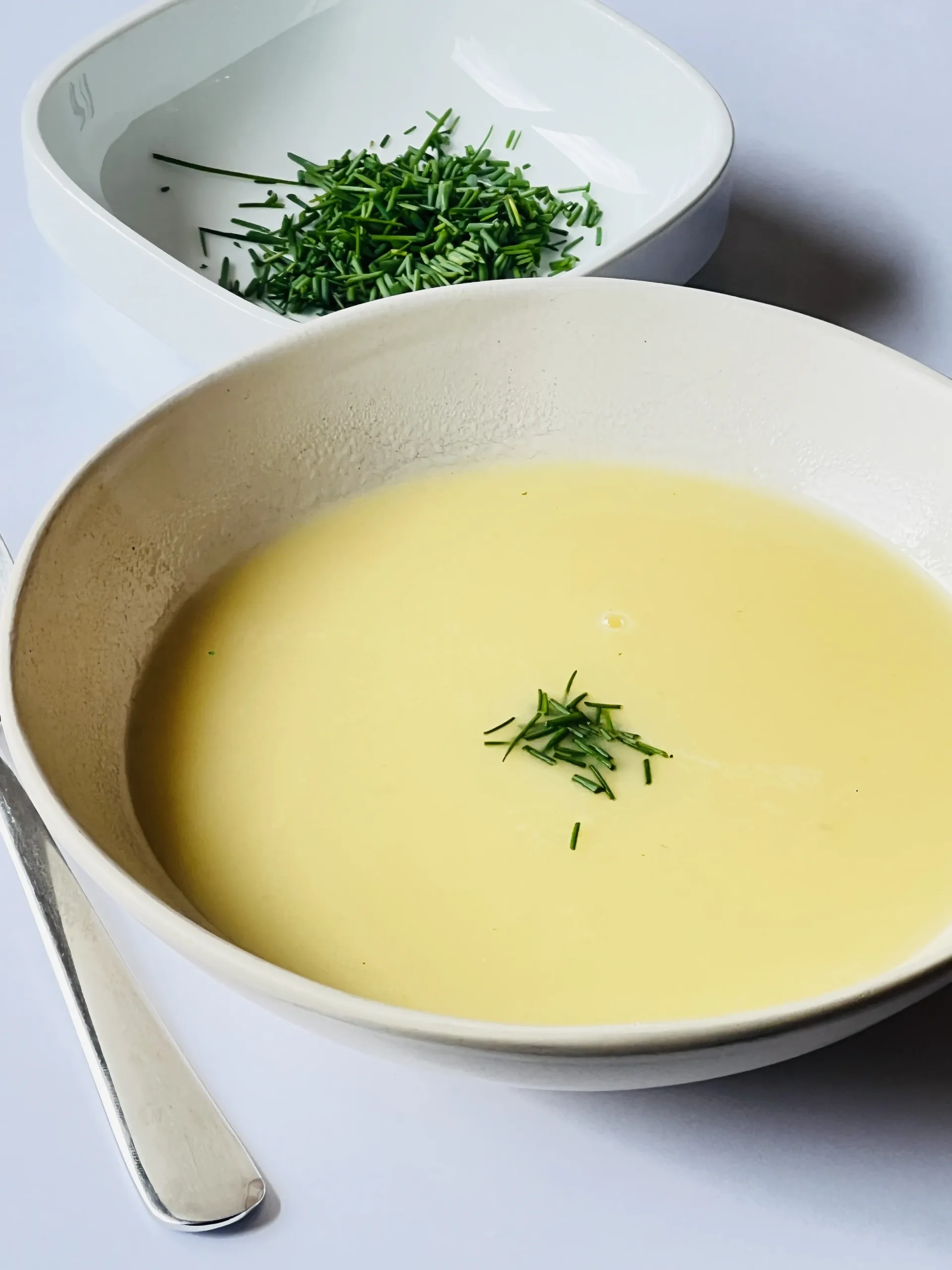 Bord romige aspergesoep met verse bieslook erover gestrooid, geserveerd op witte achtergrond