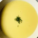 Bovenaanzicht van bord romige aspergesoep met verse bieslook erover gestrooid, geserveerd op witte achtergrond