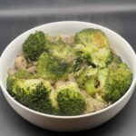 Geroerbakte broccoli met champignons in een pan, afgewerkt met een vleugje peper en peterselie, onder warme keukenbelichting.