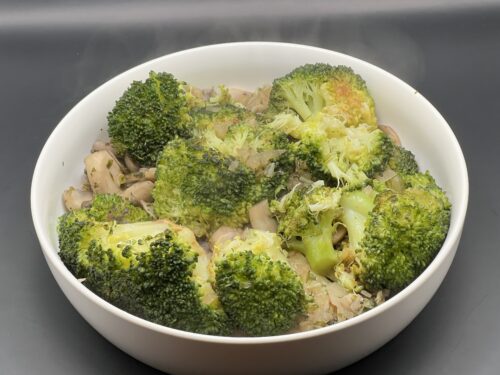 Geroerbakte broccoli met champignons in een pan, afgewerkt met een vleugje peper en peterselie, onder warme keukenbelichting.