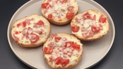 Vier halve pistolets belegd met tomaat, hesp en gesmolten mozzarella — pistolet pizza’s vers uit de oven