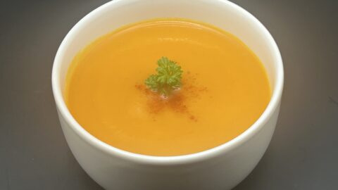 Kom warme wortelsoep met gember en kurkuma, afgewerkt met een takje peterselie en een vleugje cayennepoeder
